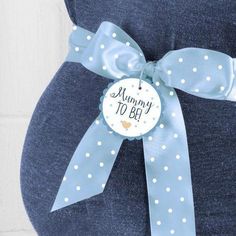 a pregnant woman's belly with a blue polka dot bow and mommy to be badge on it