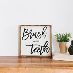 a wooden sign that says brush your teeth on it next to a potted plant