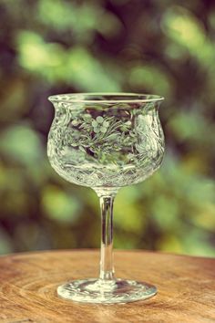 a wine glass sitting on top of a wooden table next to a forest filled with trees