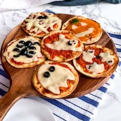 mini pizzas with cheese and black olives are on a wooden platter, ready to be eaten