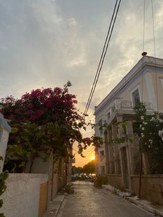 the sun is setting over an alley way with flowers growing on it and buildings in the background