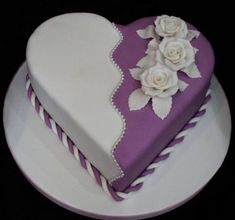 a heart shaped cake decorated with white flowers on a purple and white platter that is sitting on a black surface