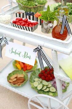 an assortment of salads and condiments are displayed on a white cart with black ribbons