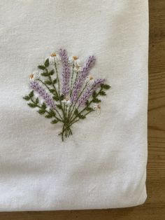 a white towel with some purple flowers embroidered on the front and side, sitting on top of a wooden table