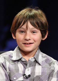 a young boy sitting in front of a microphone and smiling at the camera with his hand on his chest