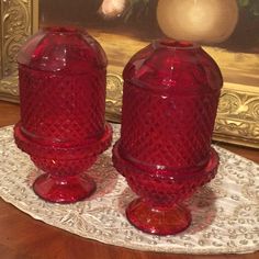 two red glass jars sitting on top of a doily