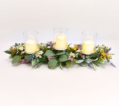 three candles sitting on top of flowers and greenery