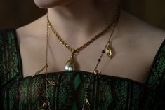 a close up of a woman wearing a green dress with gold necklaces on her neck