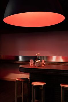 a bar with three stools and a round light hanging from the ceiling