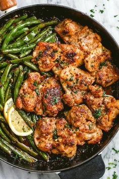 chicken and asparagus in a skillet with lemon wedges