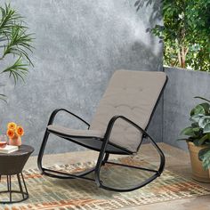 a rocking chair and table on a patio with potted plants in the back ground