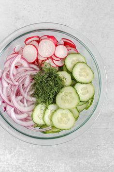 a glass bowl filled with sliced cucumbers and onions