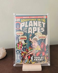 a comic book on a wooden stand with a white wall in the background and a rock next to it