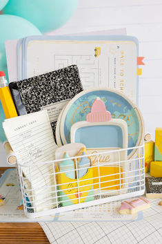 a basket filled with lots of items on top of a wooden table next to balloons