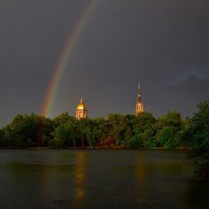 two rainbows in the sky over a lake with trees and buildings behind it at night