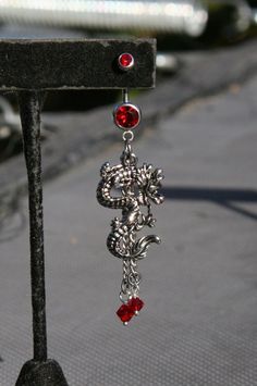 a pair of red and silver earrings hanging from a black stand on the street with cars in the background