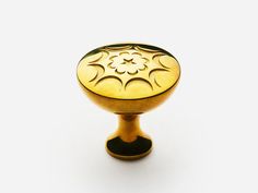 a golden cabinet knob with an intricate design on the top and bottom, against a white background