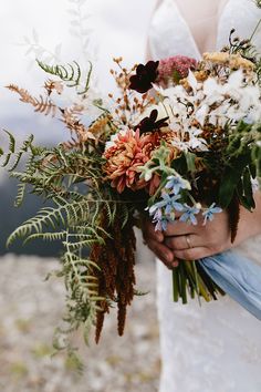 a bride holding a bouquet of flowers in her hands on top of a mountain side