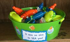 a green bucket filled with plastic toys on top of a wooden floor next to a sign that says it was so nice to sea you