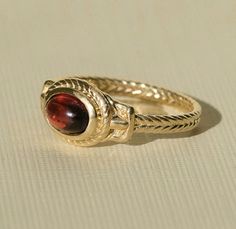 a gold ring with a red stone in the center on a white tablecloth background