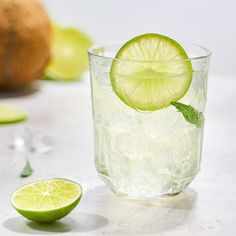 a glass filled with ice and limes next to a cut up kiwi fruit