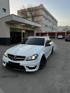 a white mercedes c - class parked in a parking lot next to some tall buildings