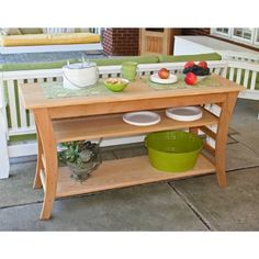 a wooden table with plates and bowls on it sitting in front of a porch area