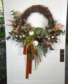 a wreath is hanging on the door with fall foliages and pumpkins around it