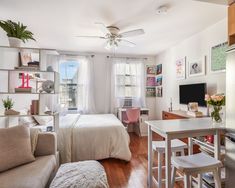 a living room with a bed, desk and television in the corner next to a window