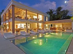 an outdoor swimming pool next to a large house at night with lights on the windows