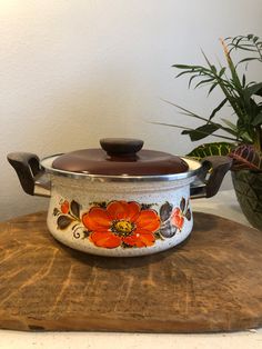 a pot with an orange flower painted on it sitting on top of a wooden table