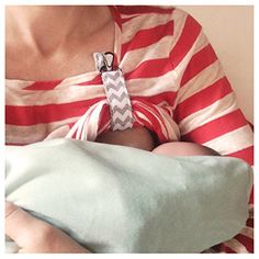 a woman holding a baby wrapped in a red and white striped shirt with a pacifier attached to it's breast