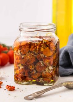 a jar filled with lots of food next to a spoon and some tomatoes on the table