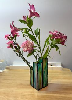 a vase with pink flowers in it sitting on a table next to a glass vase