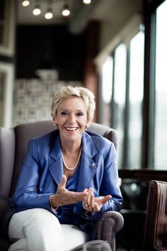 a woman sitting in a chair with her hand up to the side and smiling at the camera