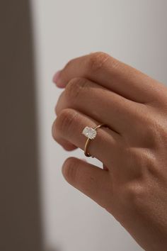 a woman's hand with a diamond ring on top of her finger, in front of a white wall