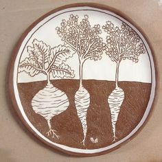 a brown and white plate with three carrots on the front, two trees in the back