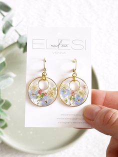 a hand holding up a pair of earrings with flowers on it and gold hoops