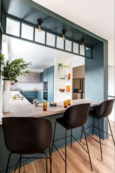 a kitchen with blue walls and black chairs in front of an island counter topped with two vases filled with flowers