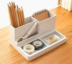 a white desk organizer with pencils, tape and scissors in it on a wooden table