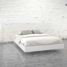 a white bed sitting next to a brick wall