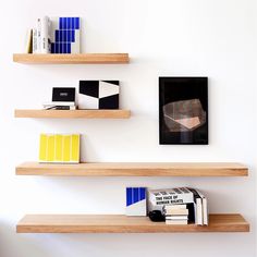 three wooden shelves with books on them against a white wall