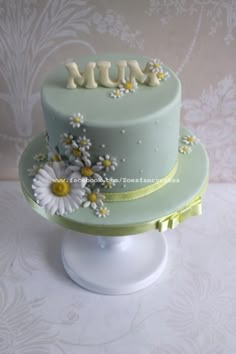 a blue cake with daisies and the word mum on top is sitting on a pedestal