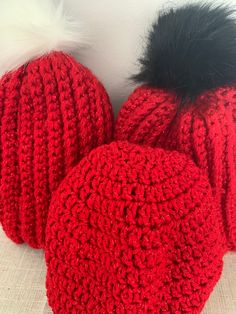 two crocheted red hats with black fur pom - poms on top