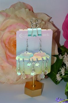 a pair of earrings on a stand with flowers in the background and a pink rose