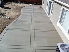 a concrete walkway in front of a house with an air conditioner on the side