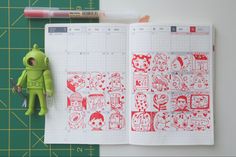 an open notebook with red and white doodles on it next to a green toy