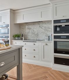 a kitchen with white cabinets and marble counter tops, an island in the middle is surrounded by wood flooring