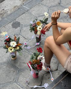 a woman sitting on a bench eating food next to flower vases with flowers in them