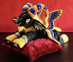 a stuffed animal sitting on top of a red pillow with wings flying above its head